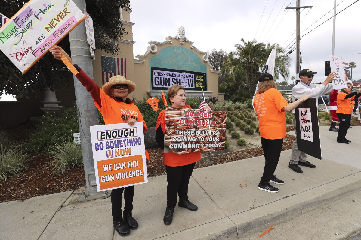 Simone MaClellan, left, and Rose Ann Sharp, second from left, hold signs as they and other people opposing the Crossroads of the West Gun Show protest at the intersection Via De La Valle and Jimmy Durante Boulevard on Saturday.