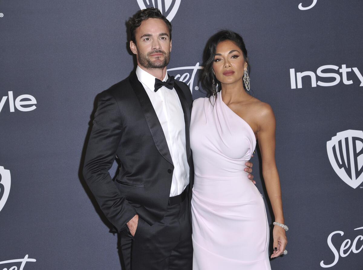 A man with dark hair and facial hair in a tuxedo standing to the left of Nicole Scherzinger in a pink one-shoulder gown