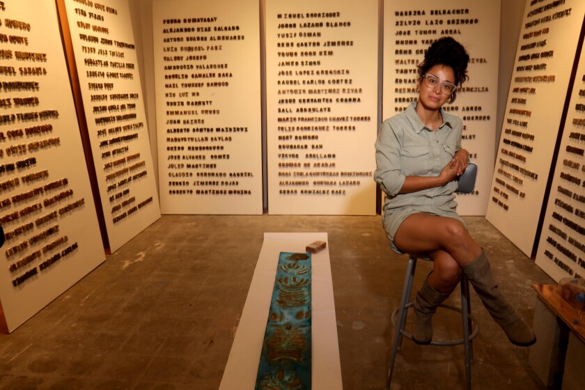 An artist is seated among seven panels covered in words.