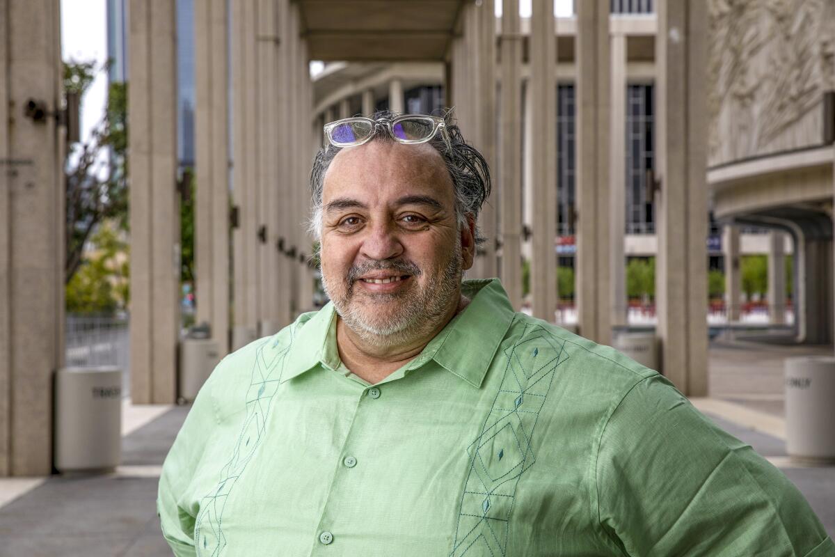 A man in a green shirt, with glasses pushed up on his forehead, poses for a photo outside at the Music Center.