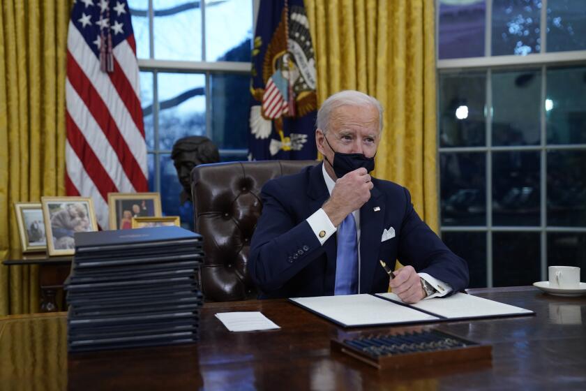 President Joe Biden adjusts his face mask as he signs his first executive orders in the Oval Office of the White House on Wednesday, Jan. 20, 2021, in Washington. (AP Photo/Evan Vucci)