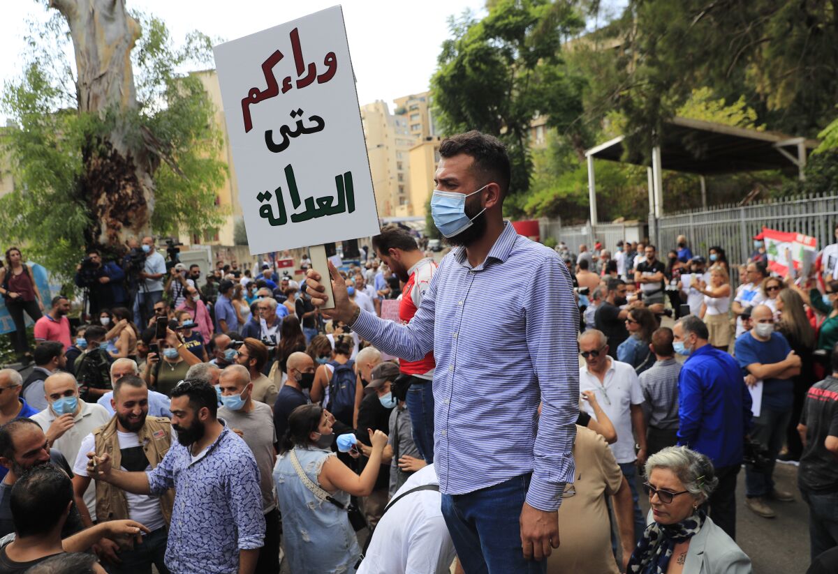 A protester holds an Arabic placard that reads: "Behind you until the justice," outside a court building during a demonstration of solidarity with Judge Tarek Bitar who is investigating last year's deadly seaport blast, in Beirut, Lebanon, Wednesday, Sept. 29, 2021. Hundreds of Lebanese, including families of the Beirut port explosion victims, rallied Wednesday outside the court of justice in support of Bitar after he was forced to suspend his work. Bitar is the second judge to take on the complicated investigation.(AP Photo/Hussein Malla)