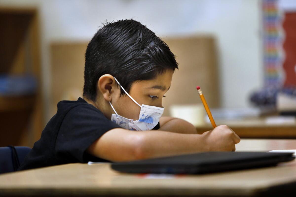 A young child wears a mask in a classroom