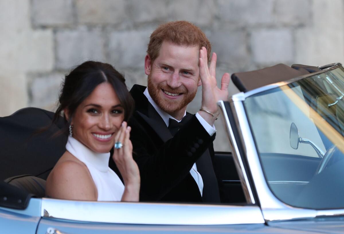 Prince Harry and Meghan Markle wave from inside a convertible.