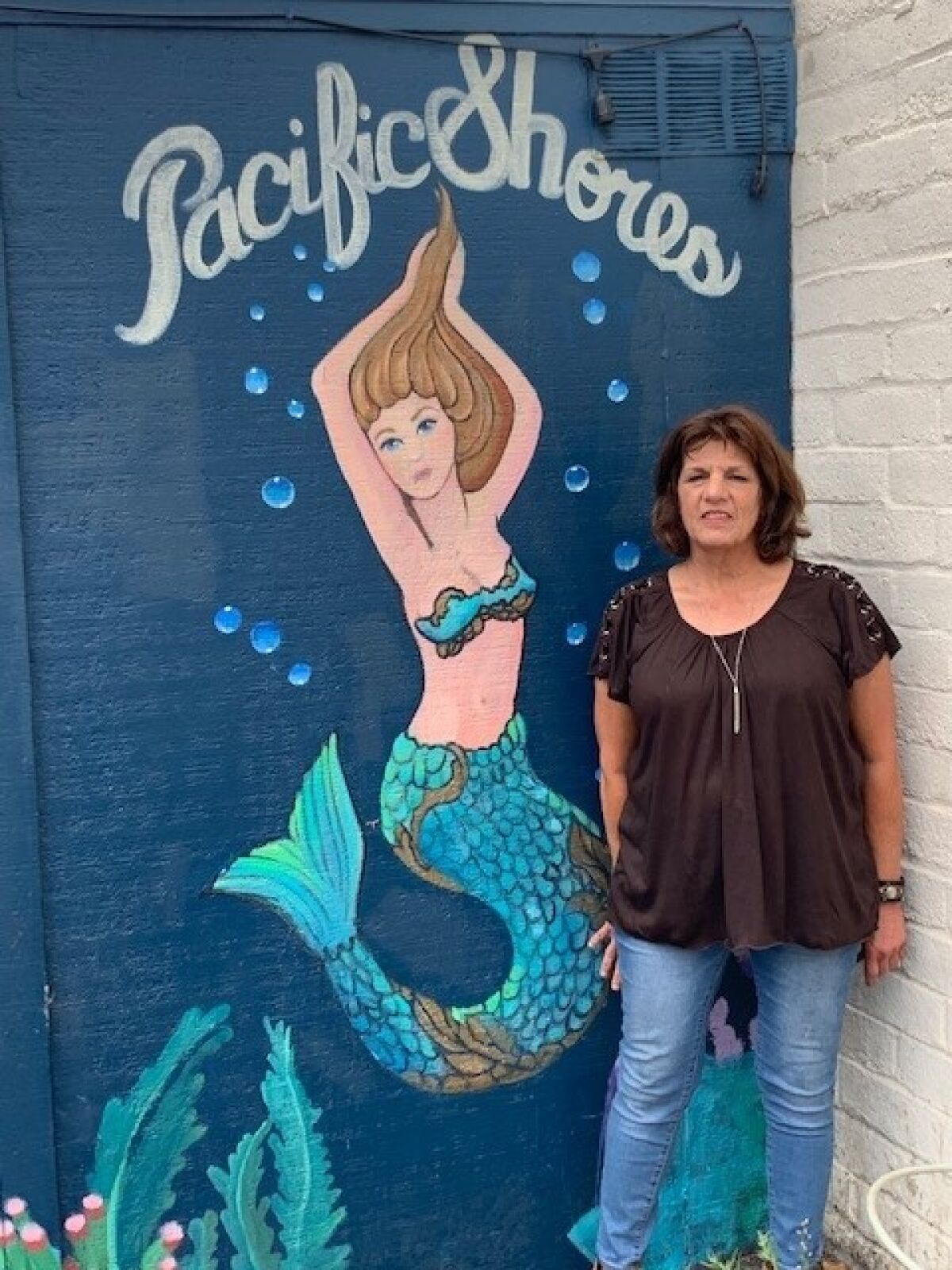 Artist Janis Ambrosiani stands beside a mermaid mural she created in Ocean Beach.
