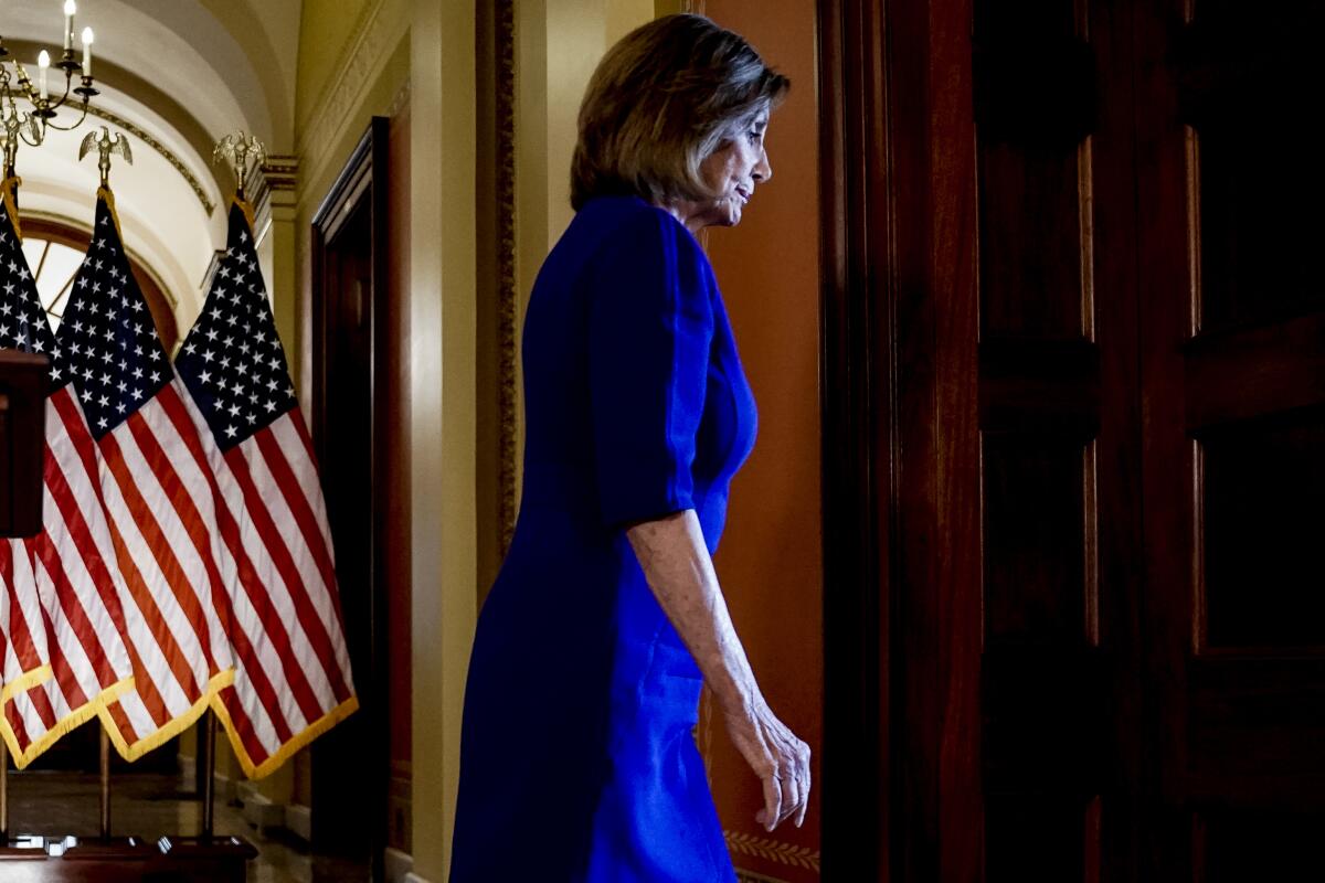 House Speaker Nancy Pelosi walks away from a podium with U.S. flags in the background
