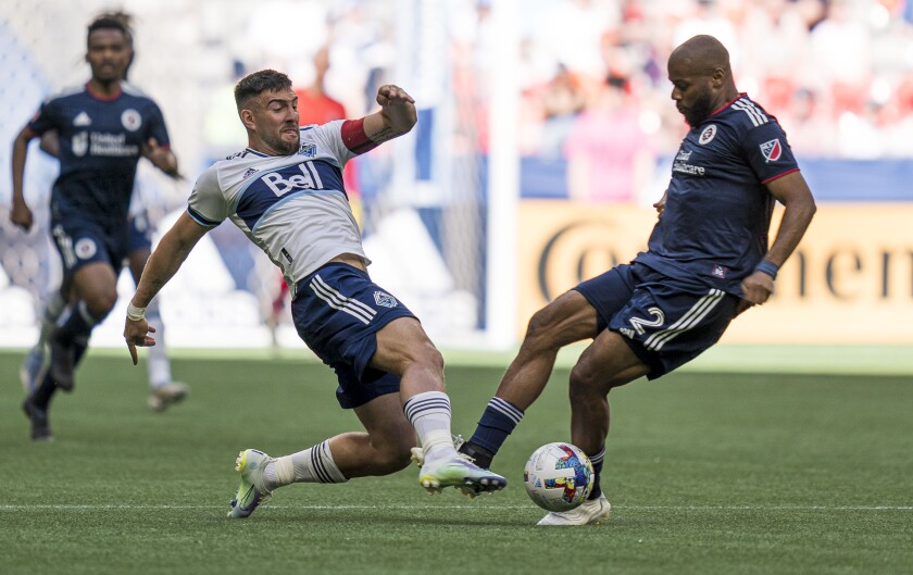 Vancouver Whitecaps' Lucas Cavallini, left, tries to push the the ball past New England Revolution's Andrew Farrell during first-half MLS soccer match action in Vancouver, British Columbia, Sunday, June 26, 2022. (Rich Lam/The Canadian Press via AP)