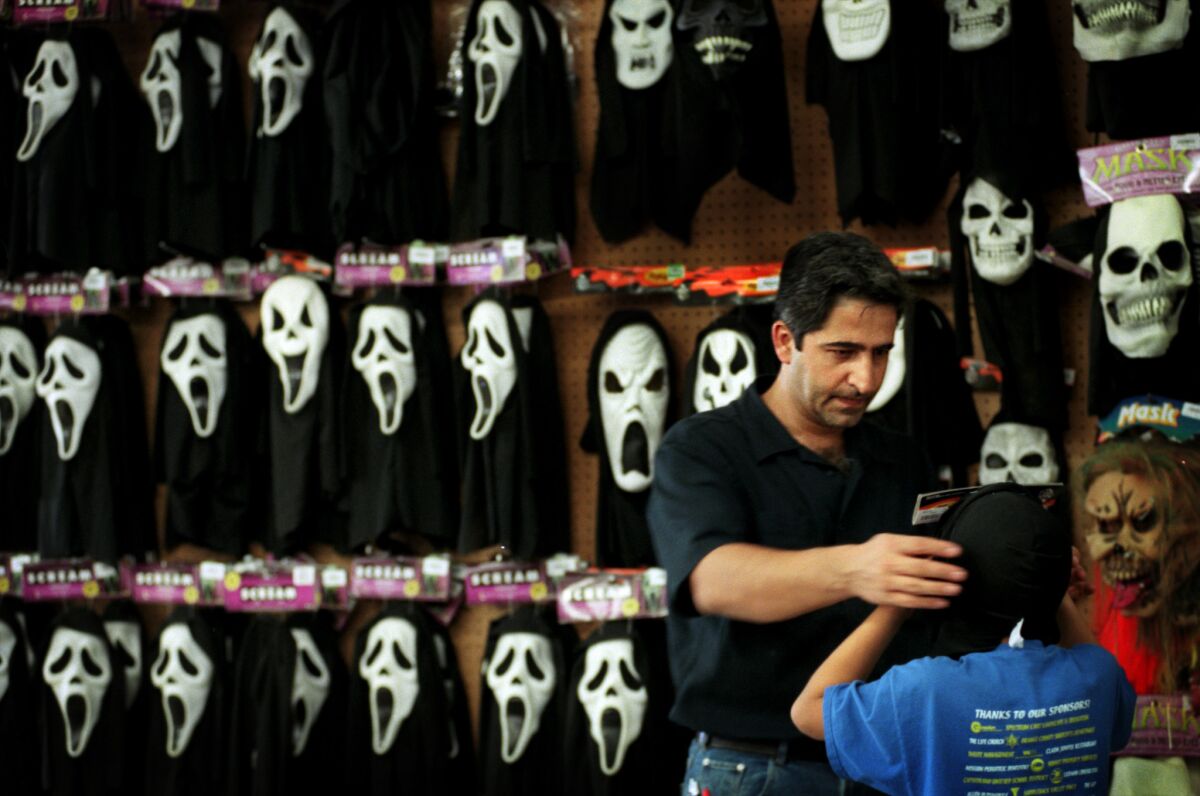 A man places a "Scream" mask on his son at a Spirit Halloween store