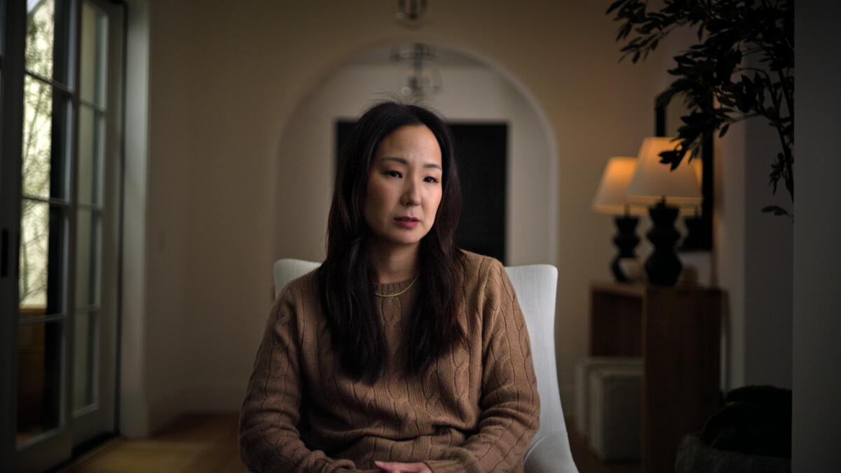 Melanie Lee, in a brown cable knit sweater, sitting on a white chair in a beige room