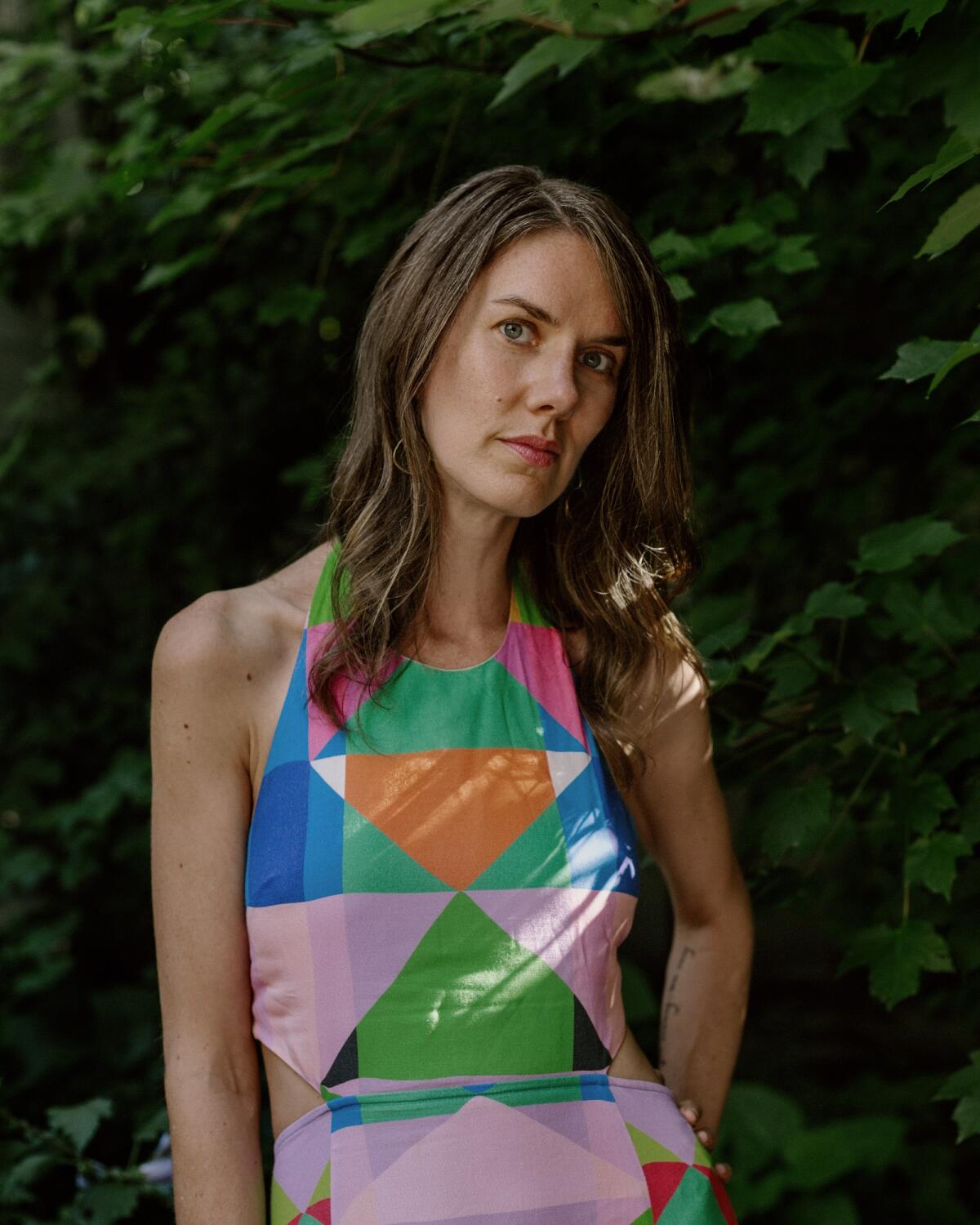 Leslie Jamison, in a colorful geometric-print dress, stands under a tree.