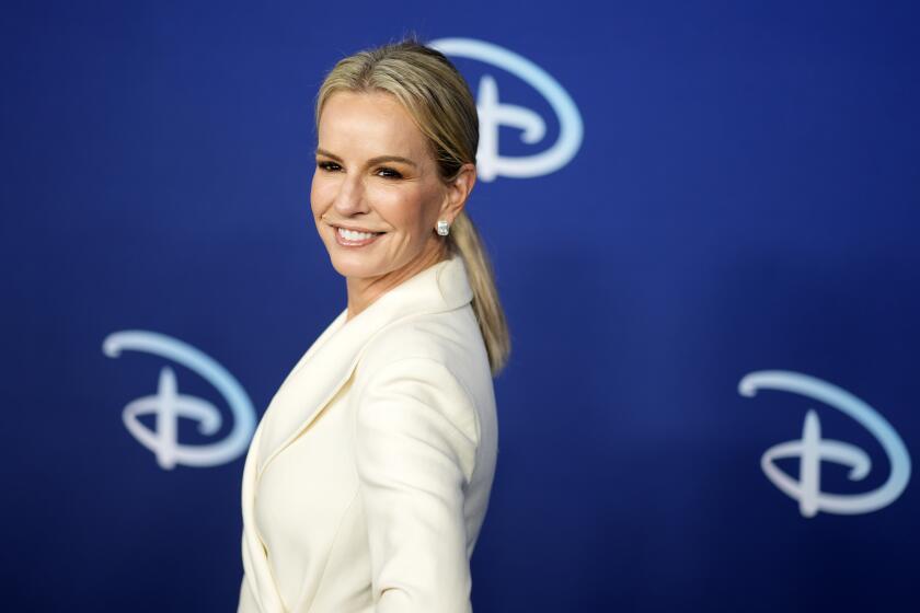 Jennifer Ashton smiling in a cream-colored suit and low ponytail in front of a blue background