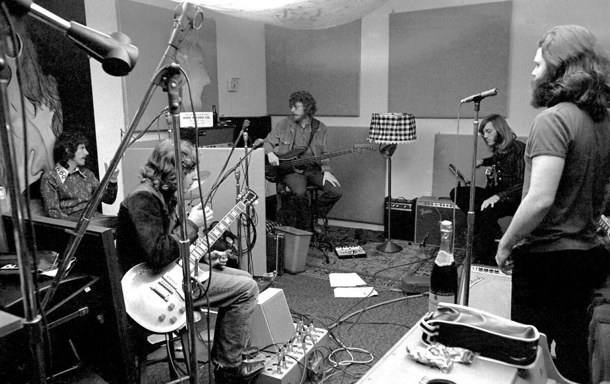 Five men holding musical instruments in a recording studio in the early 1970s