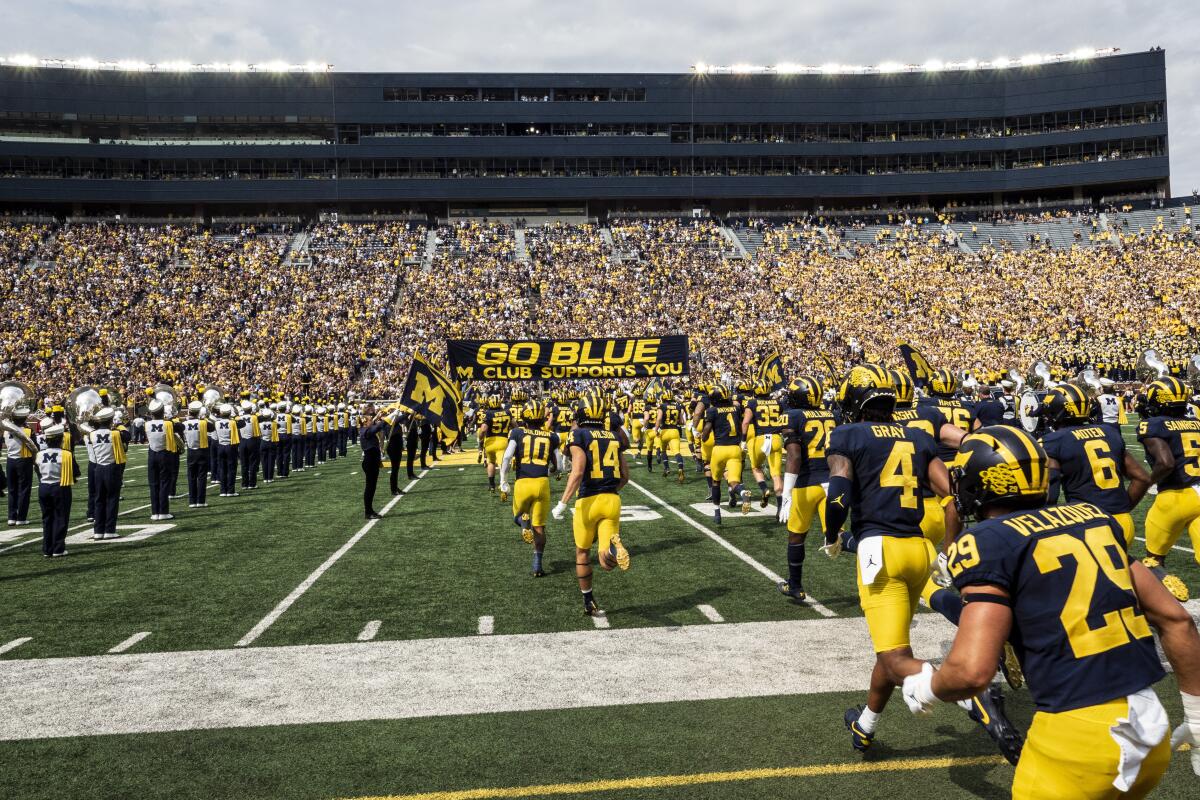 The Wolverines run onto the Michigan Stadium field under the "GO BLUE, M CLUB SUPPORTS YOU" banner on Sept. 4, 2021.