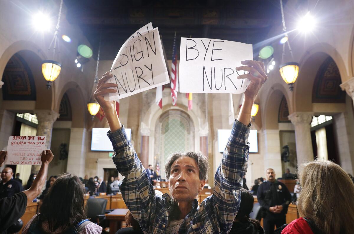 A man holding up signs calls for the resignation of council members in downtown L.A. on Oct. 12, 2022.