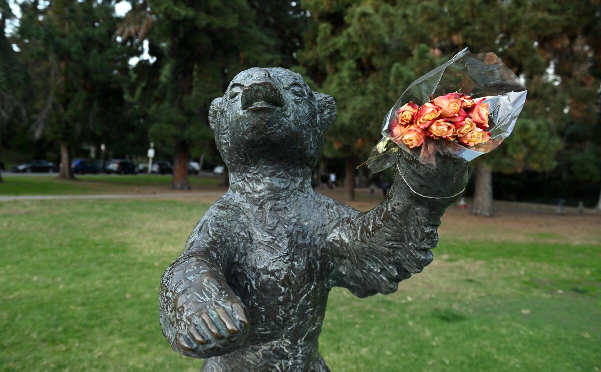 A bear statue outside holds roses