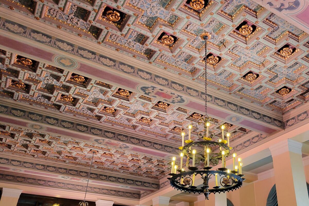 A coffered, painted ceiling from which a two-tiered chandelier hangs.