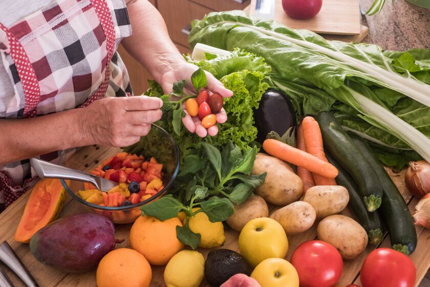 The hands of an old woman cut the fruit and look for the best small tomatoes. Wooden table with a large group of colorful fruits and vegetables. Eat healthy