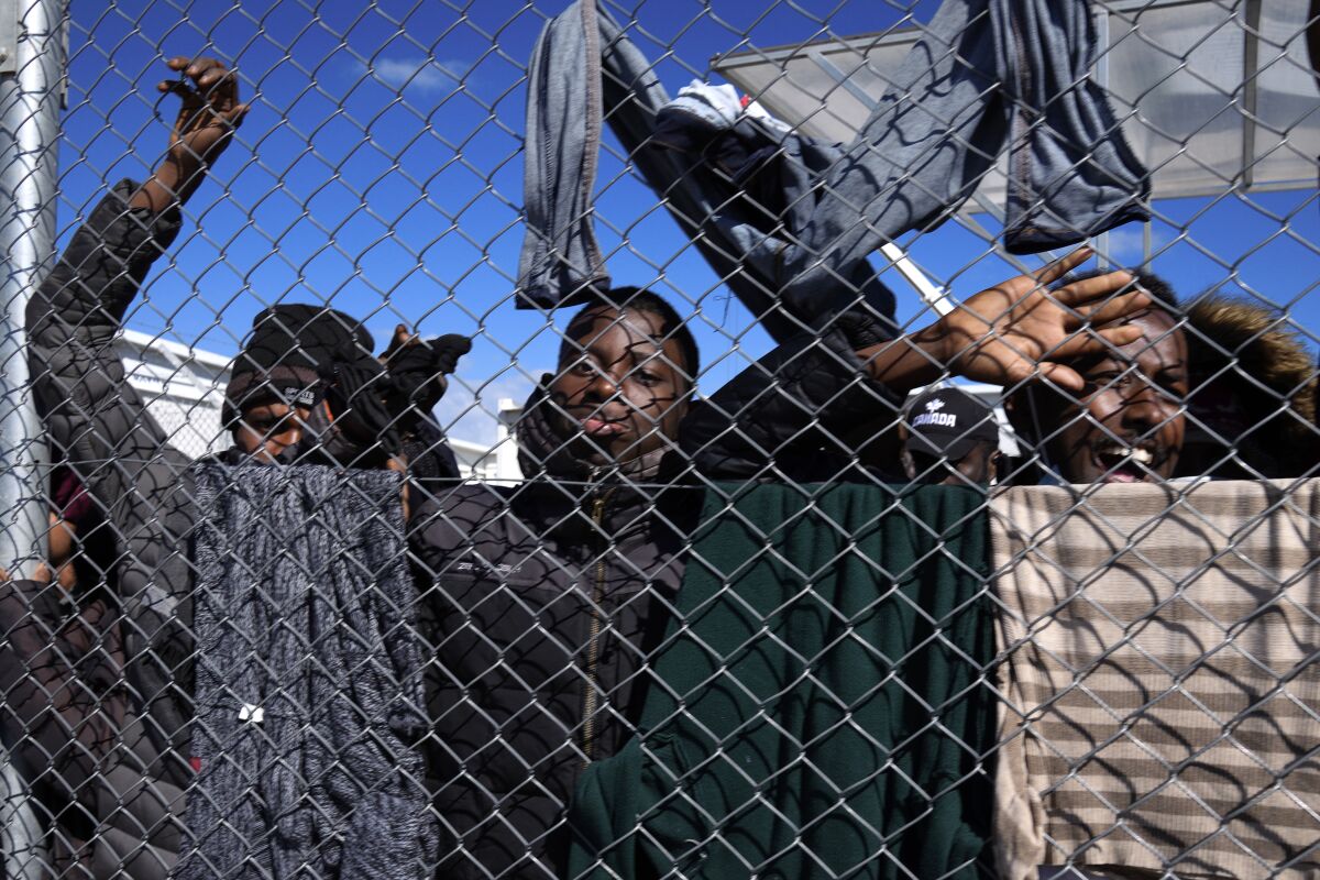 Migrants stand behind a fence during Cyprus' president Nicos Anastasiades visit the Pournara migrant reception center in Kokkinotrimithia outside of capital Nicosia, Cyprus, on Monday, March 14, 2022. Anastasiades said after wrapping up his brief visit to the overcrowded migrant reception camp that his government would work to make it there "more humane" amid criticism that living conditions for more than 350 unaccompanied minors are "miserable." (AP Photo/Petros Karadjias)