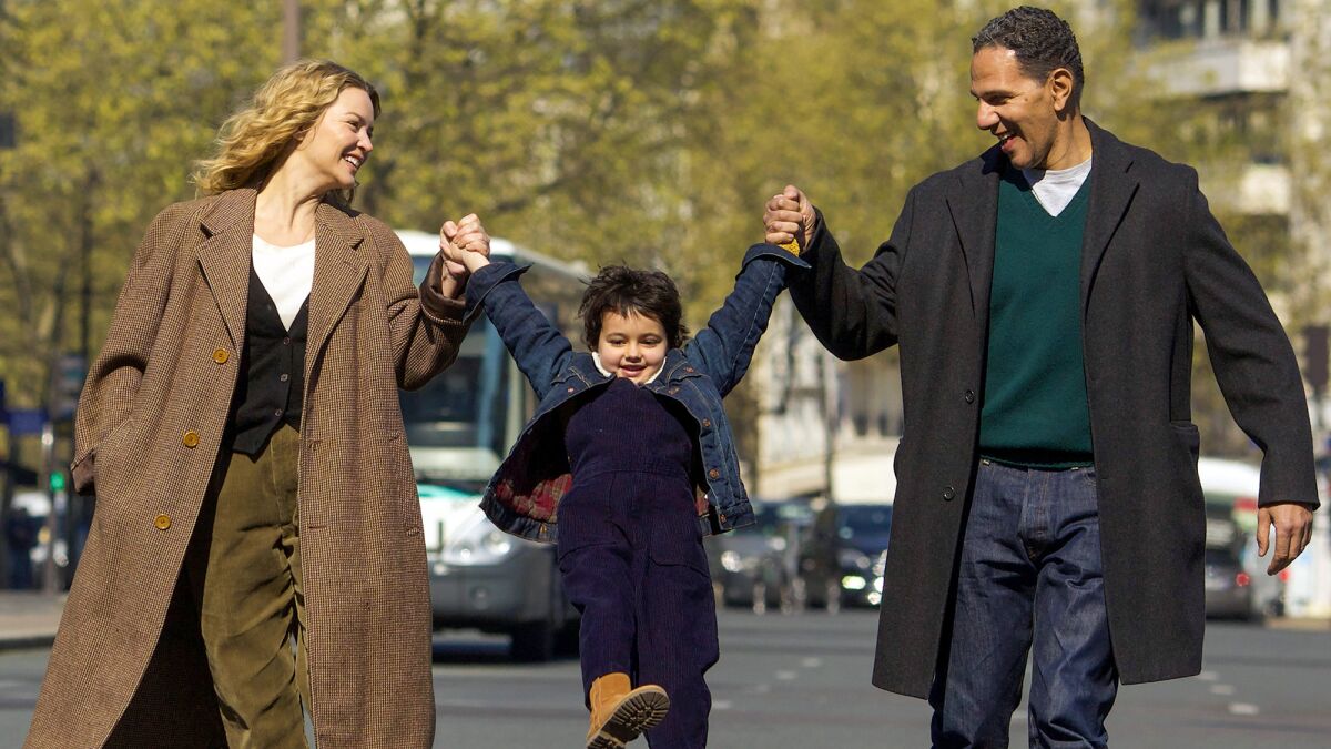 A woman, a young girl and a man link hands as they walk along a street.