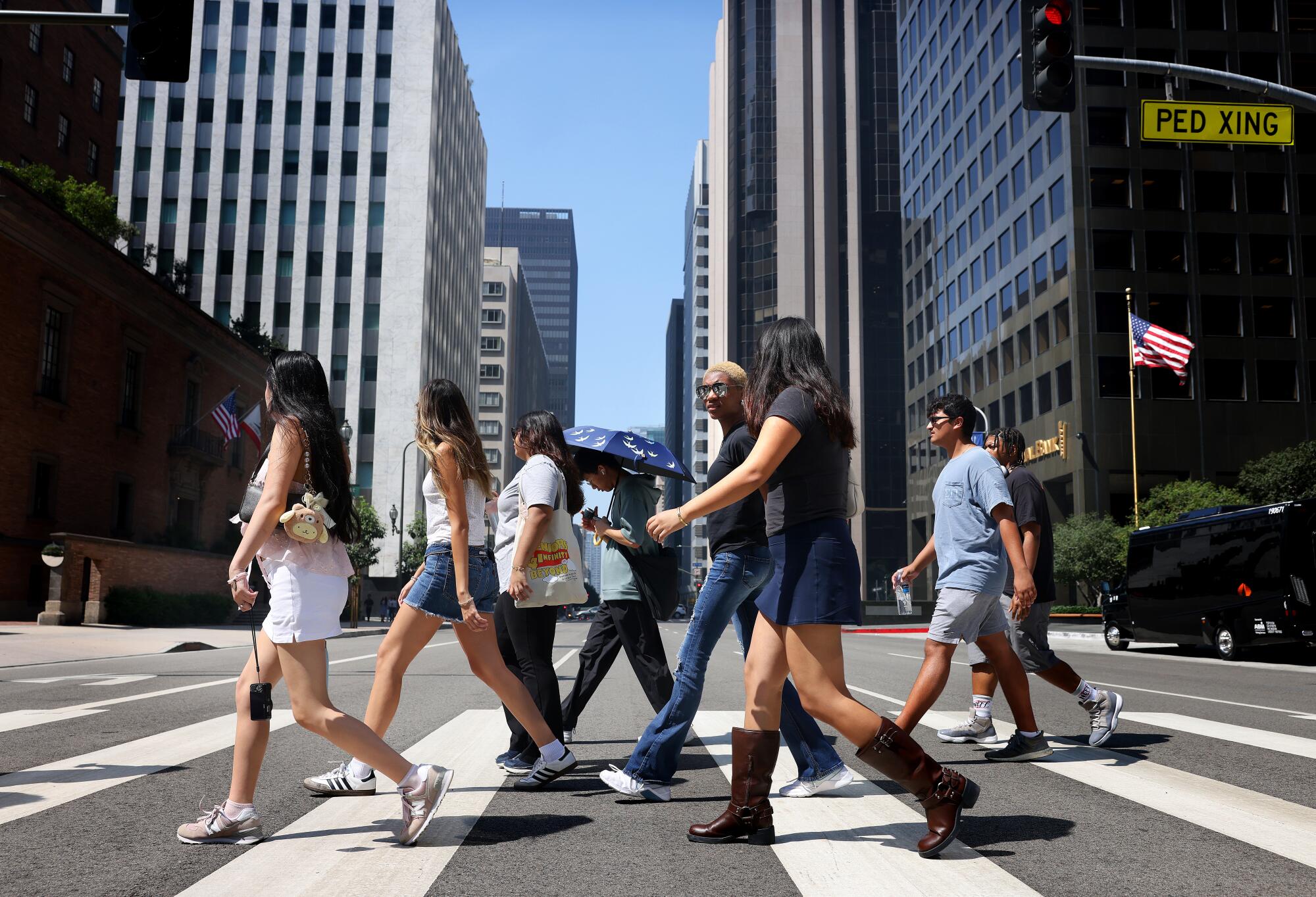 Teenagers cross a downtown Los Angeles street with skyscrapers in the background.