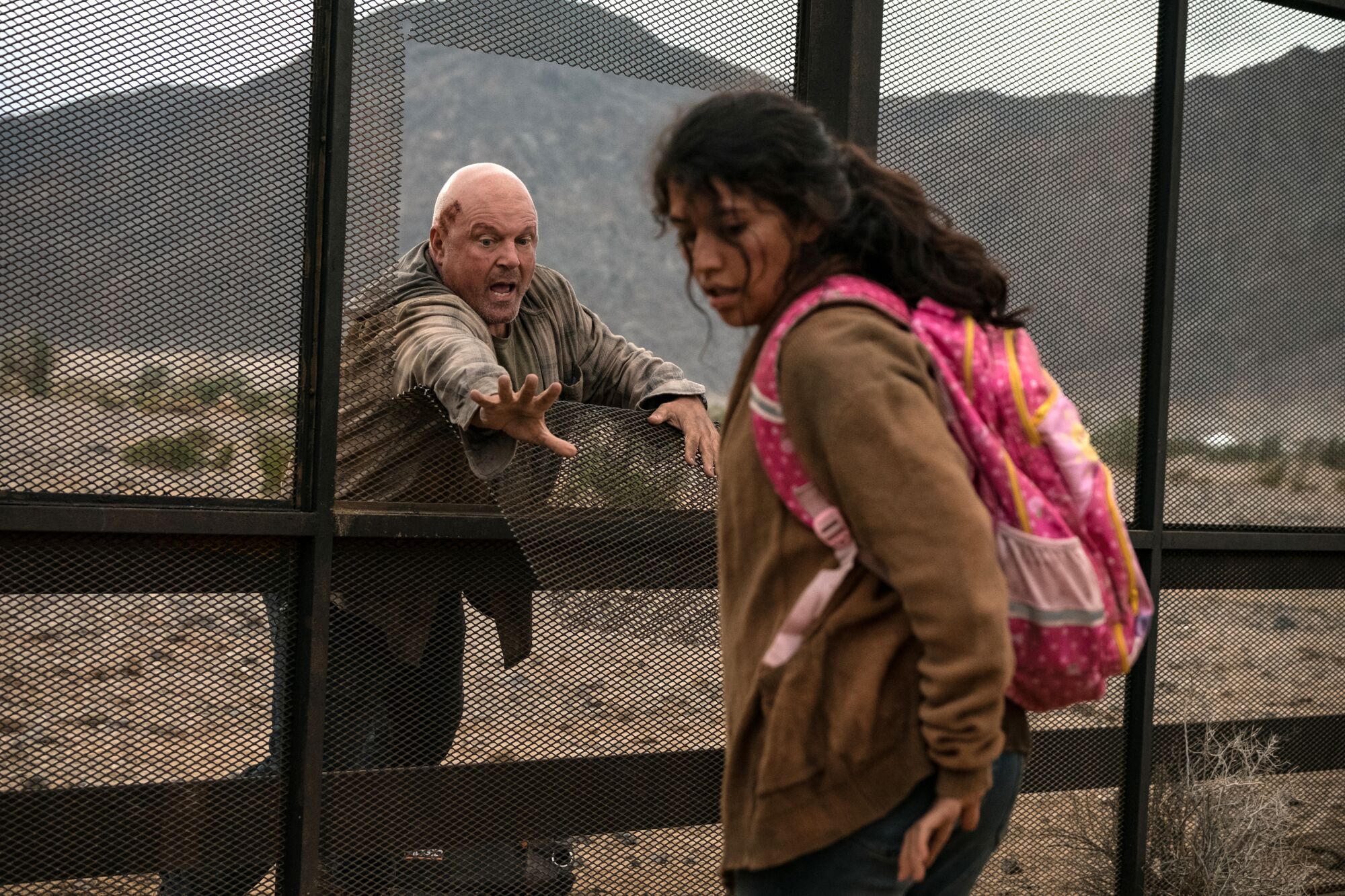 A man reaches out through a hole in a fence as a woman looks on.