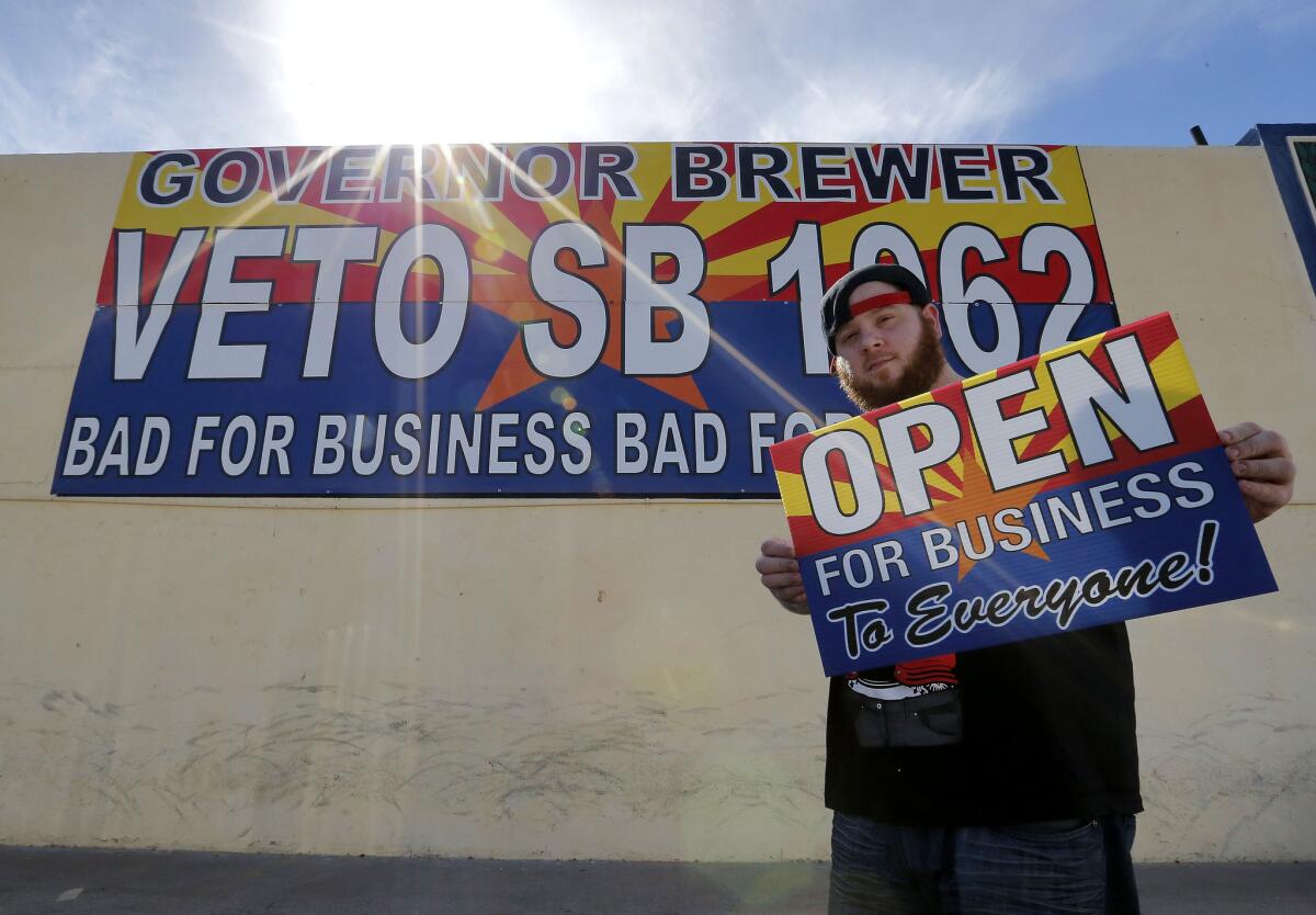 Josh Deinert, a graphic designer at Fast Signs in Phoenix, shows off a sign opposing the controversial Arizona bill SB 1062. Gov. Jan Brewer will hold a series of private meetings with opponents and proponents of legislation adding protections for people who assert their religious beliefs in refusing service to gays.