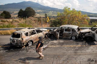 A person inspects the area where four vehicles were burned by alleged members of organized crime.