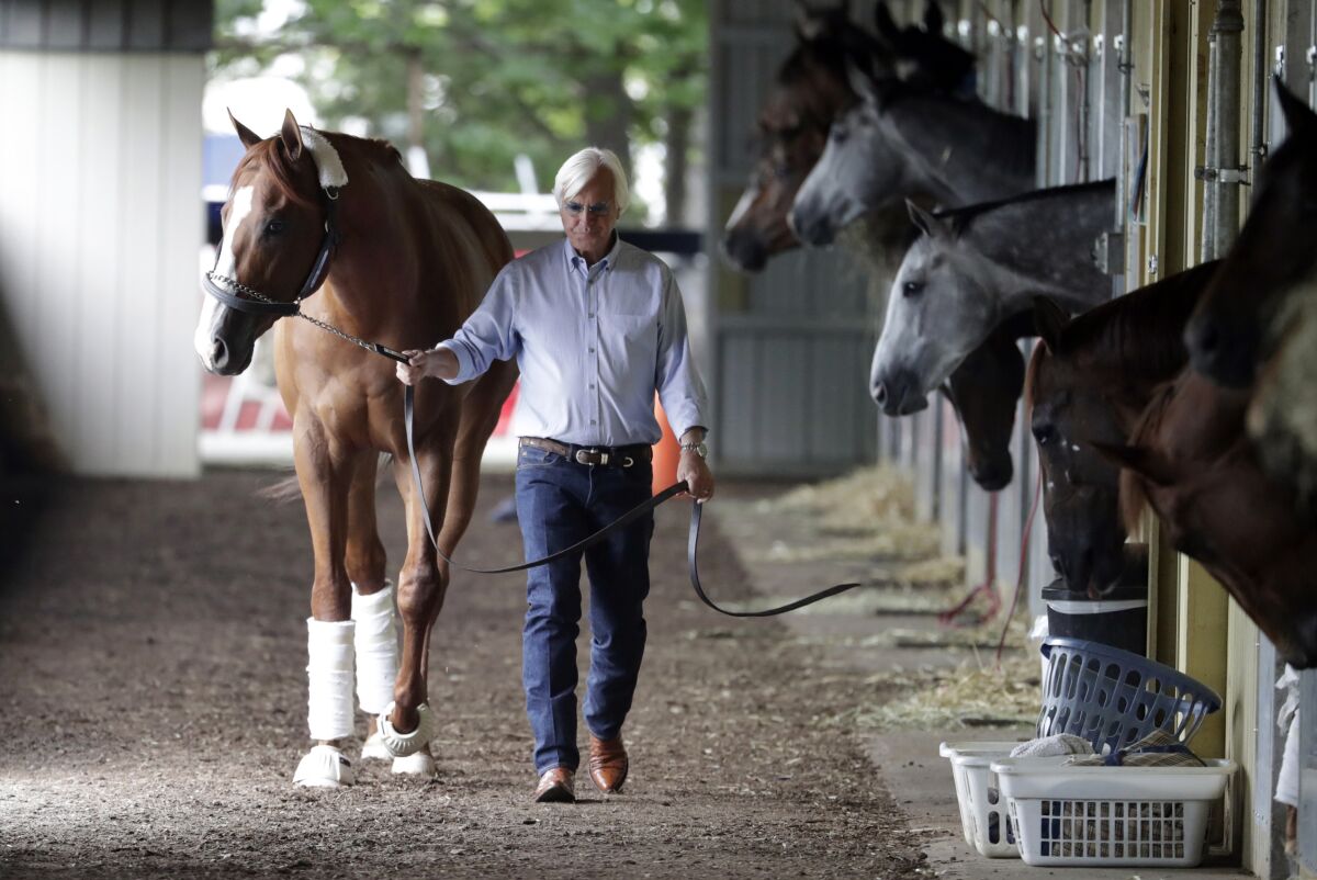 Bob Baffert walks a horse past several other horses in a stable.
