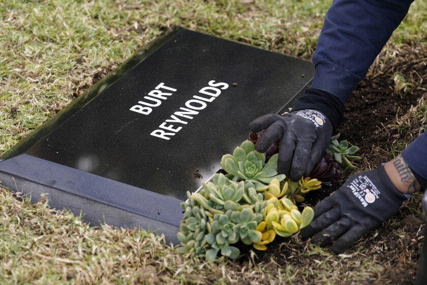 Flowers are placed in front of a temporary headstone for the late actor Burt Reynolds in the Garden of Legends section of Hollywood Forever cemetery, Thursday, Feb. 11, 2021, in Los Angeles. Reynolds' cremated remains were moved from Florida to Hollywood Forever, where a small ceremony was held Thursday. A permanent gravesite will be put up for Reynolds in a few months. (AP Photo/Chris Pizzello)