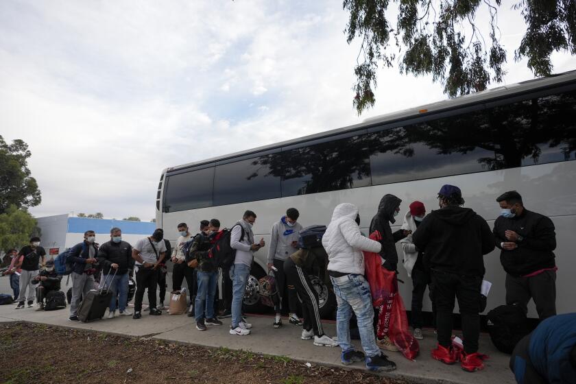 Migrantes descargan sus pertenencias de un autobús al llegar a una parada después de salir de un centro de trámites migratorios, el viernes 23 de febrero de 2024, en San Diego. (AP Foto/Gregory Bull)