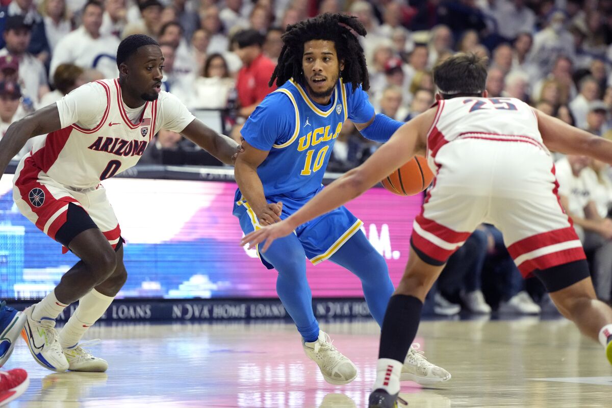 UCLA guard Tyger Campbell drives between Arizona guards Courtney Ramey, left, and Kerr Kriisa during the first half.