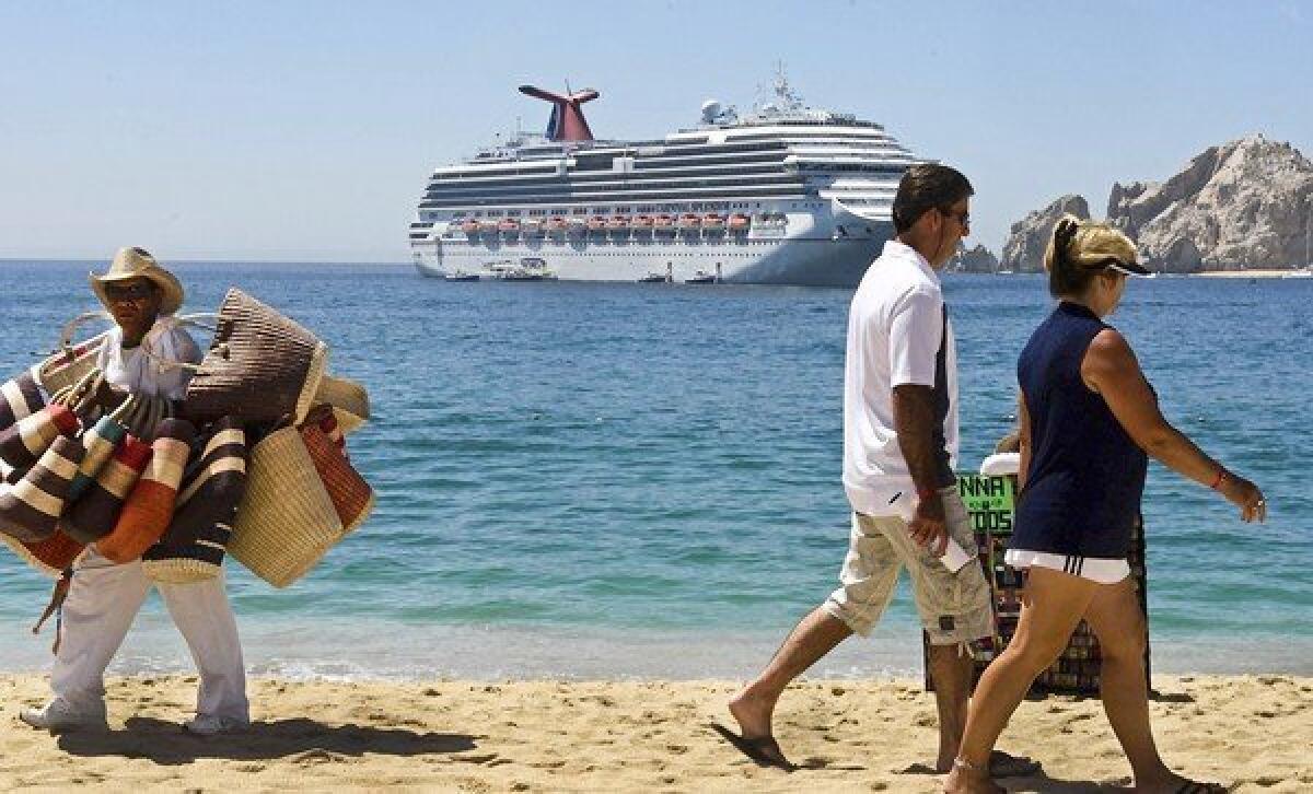 A beach vendor, left, looks for a sale as tourists walk on Medano Beach as a cruise ship is anchored offshore in Los Cabos, Baja California, Mexico.