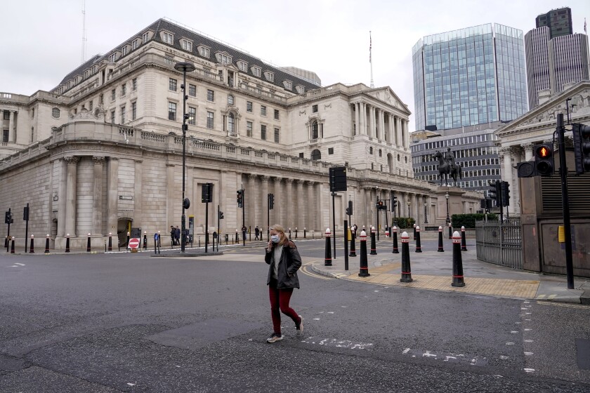 A woman wears a face mask while walking crossing a road outside the Bank of England, in the financial district, known as The City, in London, Monday, Dec. 13, 2021. While many people will re-start working from home, the British government raised the country's official coronavirus threat level on Sunday, warning the rapid spread of omicron "adds additional and rapidly increasing risk to the public and health care services" at a time when COVID-19 is already widespread. (AP Photo/Alberto Pezzali)
