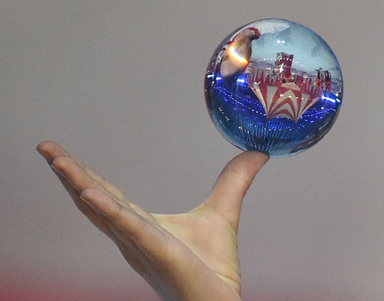 A scene of the 2014 Sochi Winter Olympics Closing Ceremony is reflected in a glass ball held by a circus performer.