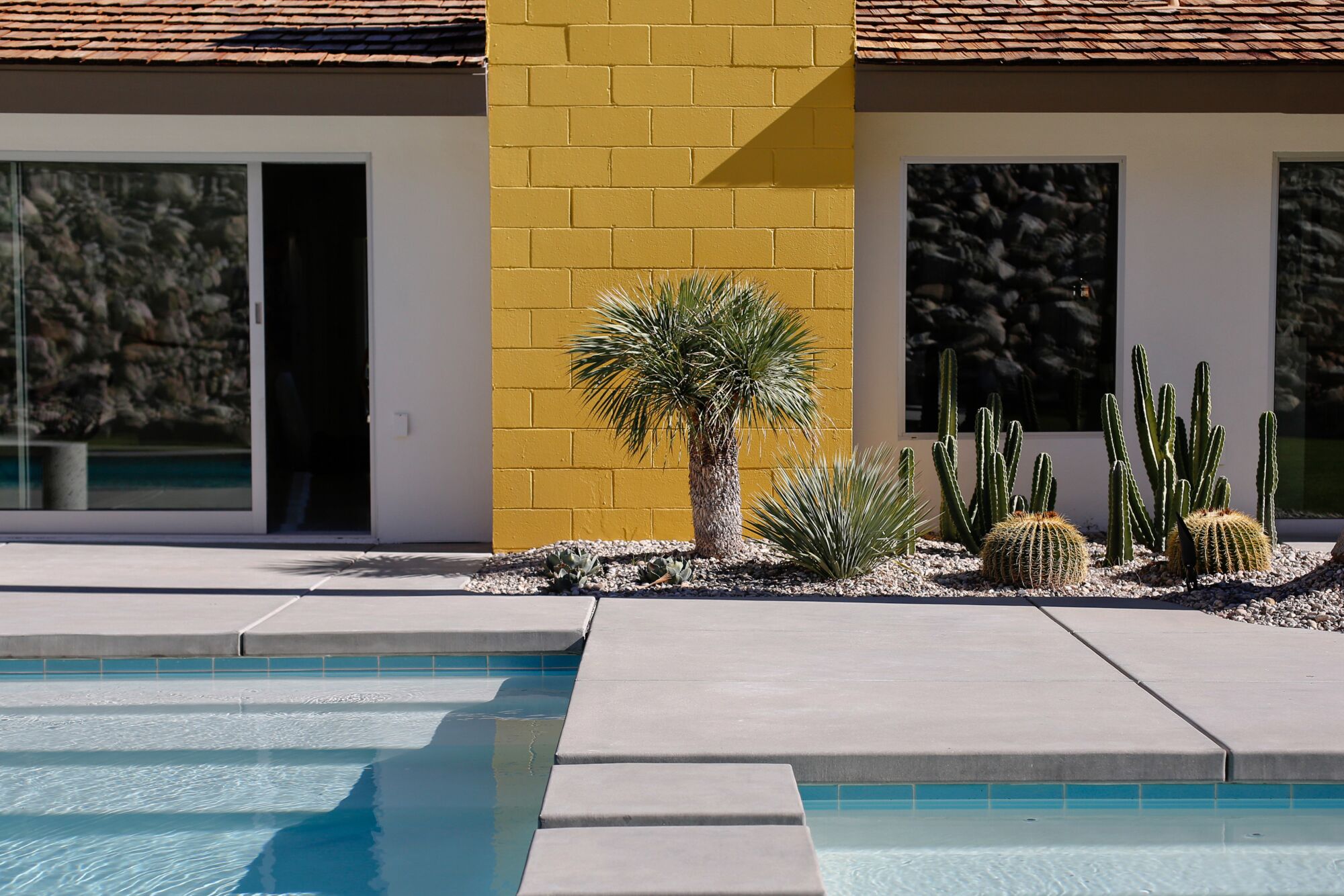 A swimming pool and cactus in the yard of a house with a yellow fireplace