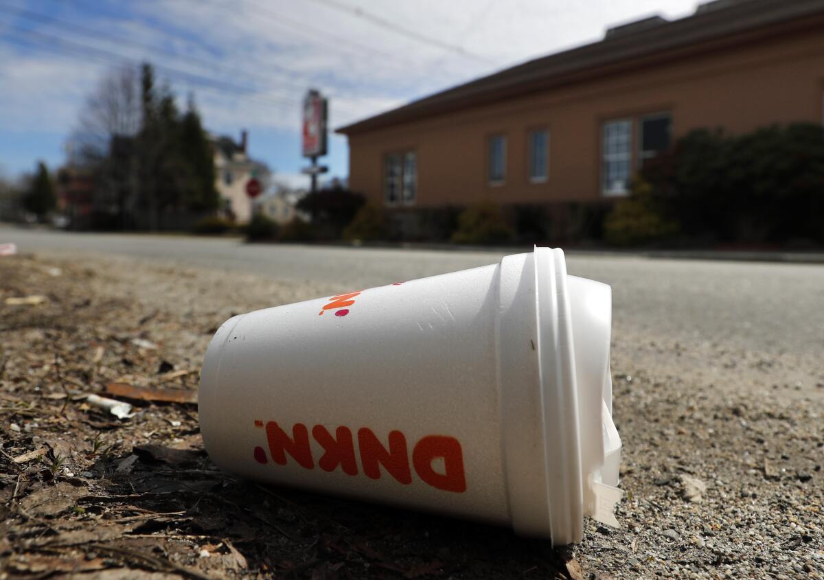 A coffee cup made from polystyrene foam lies on the side of a road