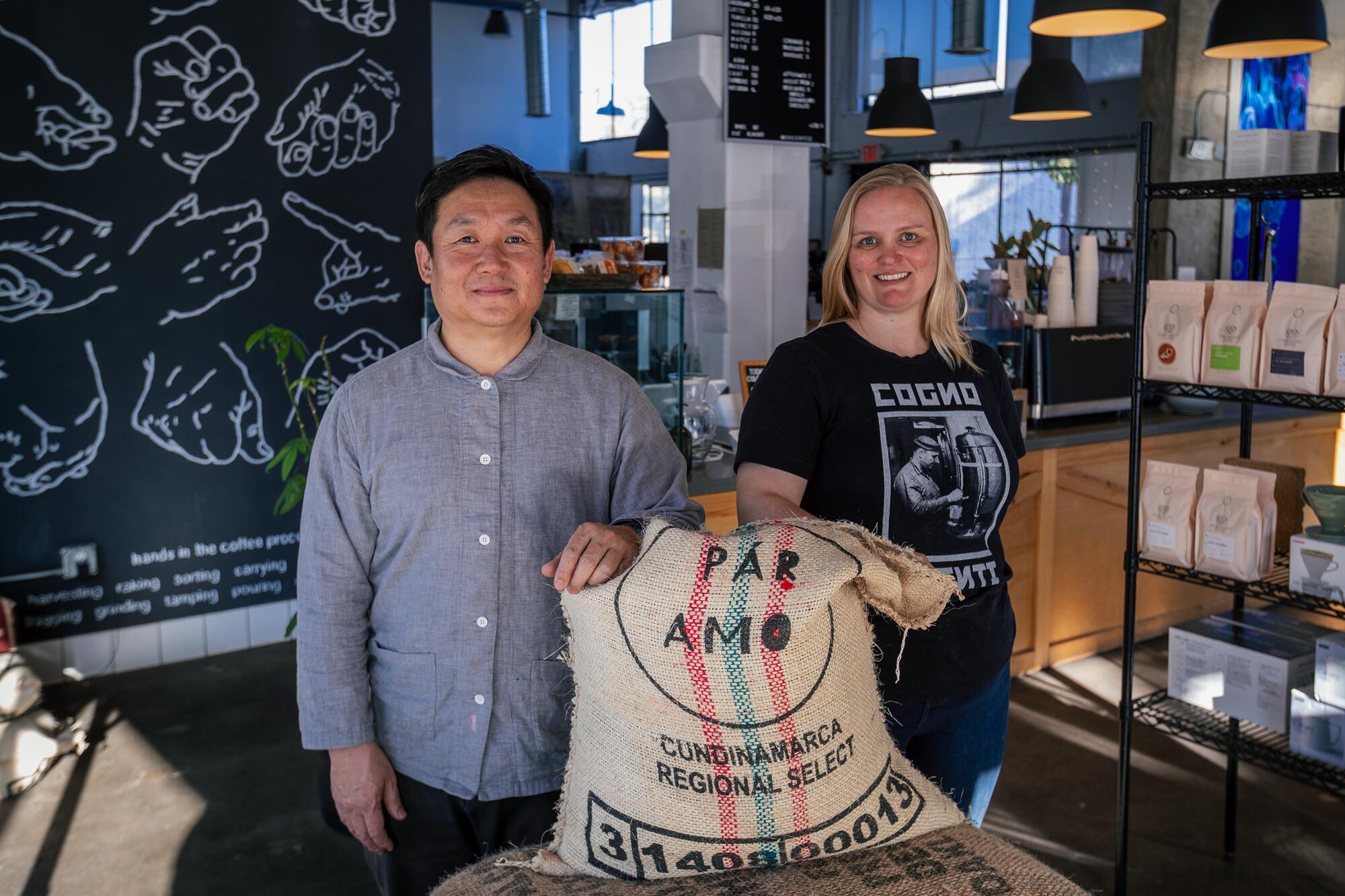 Two people in a coffee shop with a large burlap sack of coffee beans between them.