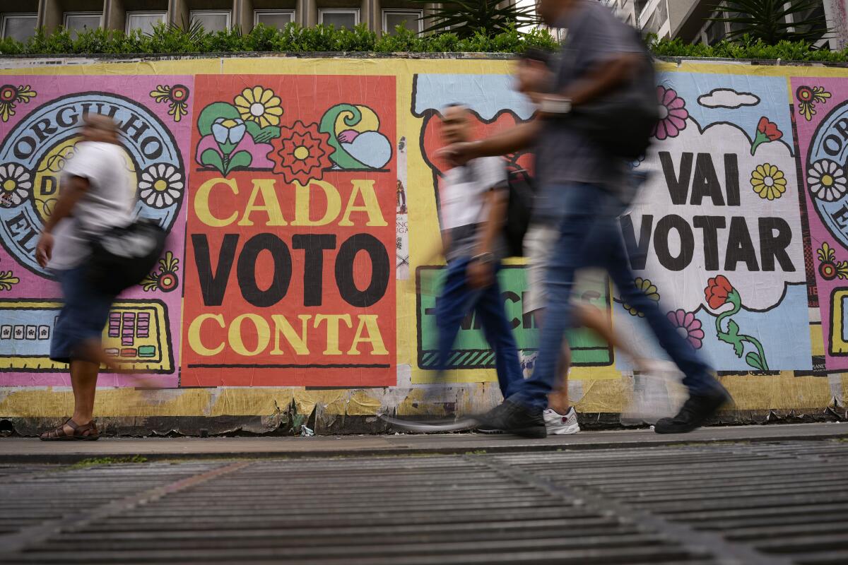 ARCHIVO - Personas caminan frente a un mural con el mensaje "Cada voto cuenta", en Sao Paulo, Brasil, 