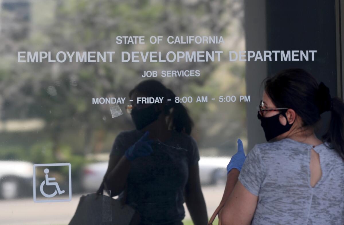 A woman in a mask and gloves stands outside a closed glass door labeled Employment Development Department Job Services