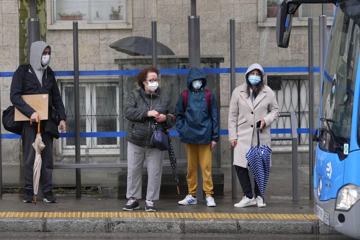 People wait with masks to protect against the spread of coronavirus before boarding a bus in Madrid, Spain, Wednesday, April 20, 2022. Spain is taking another step toward post-pandemic normality by partially ending the obligatory use of masks indoors. A government decree taking effect Wednesday keeps masks still mandatory in medical centers and in all forms of public transport. (AP Photo/Paul White)