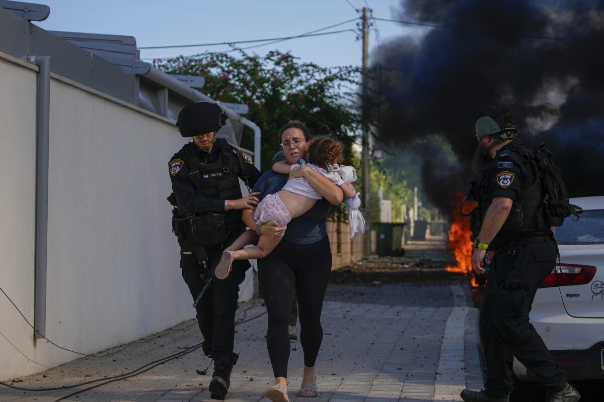 Israeli police officers evacuate a woman with a child in her arms from a site hit by rocket fire 