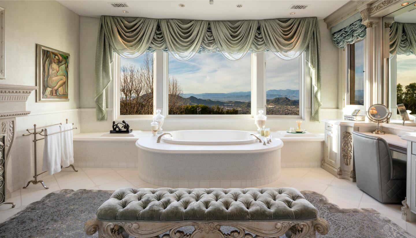 A tub dominates the primary bathroom, with large window, vanity area and fireplace.