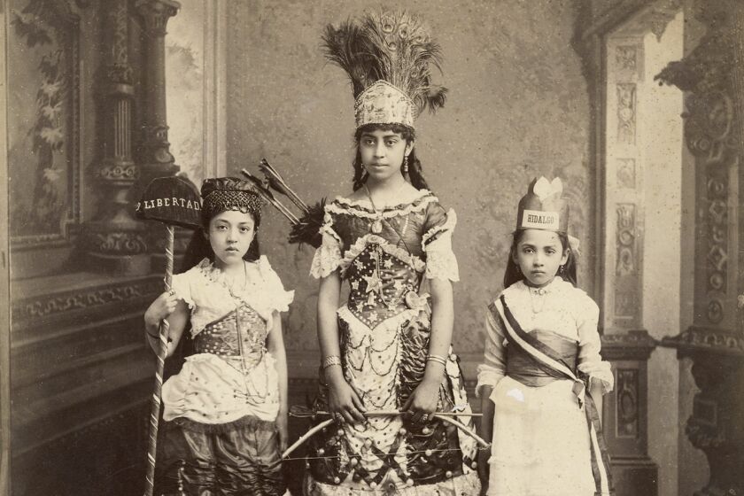 A sepia image shows three little girls in fantastical outfits, one with a headdress, in a carpeted foyer