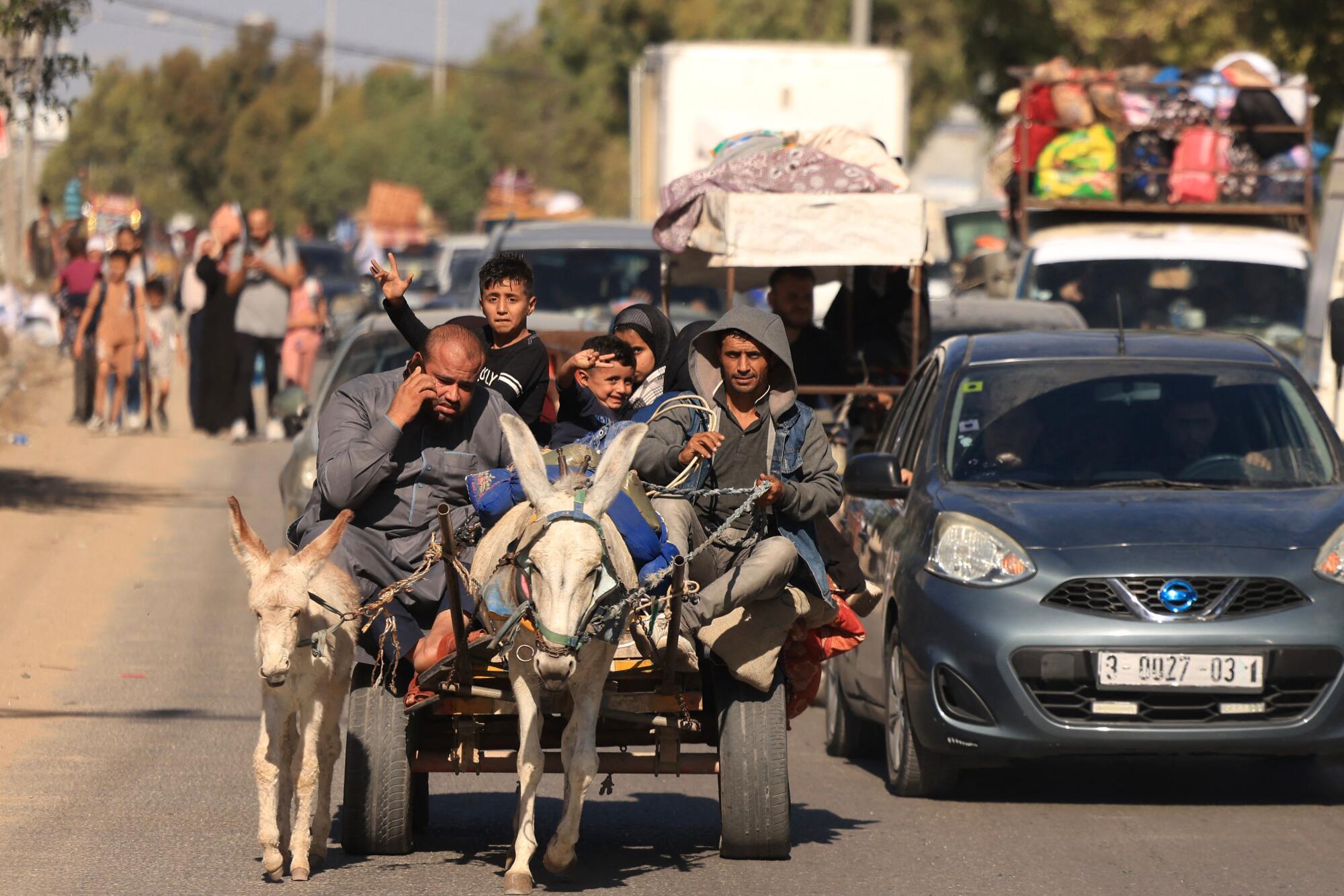 A family in a donkey-drawn cart joins cars, trucks and people on foot, all heading in the same direction on a dusty roadway