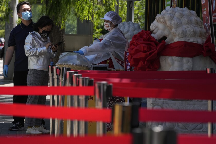 A vendor sells take away food near barriers set up to keep customers spread out on Friday, May 13, 2022, in Beijing. (AP Photo/Ng Han Guan)