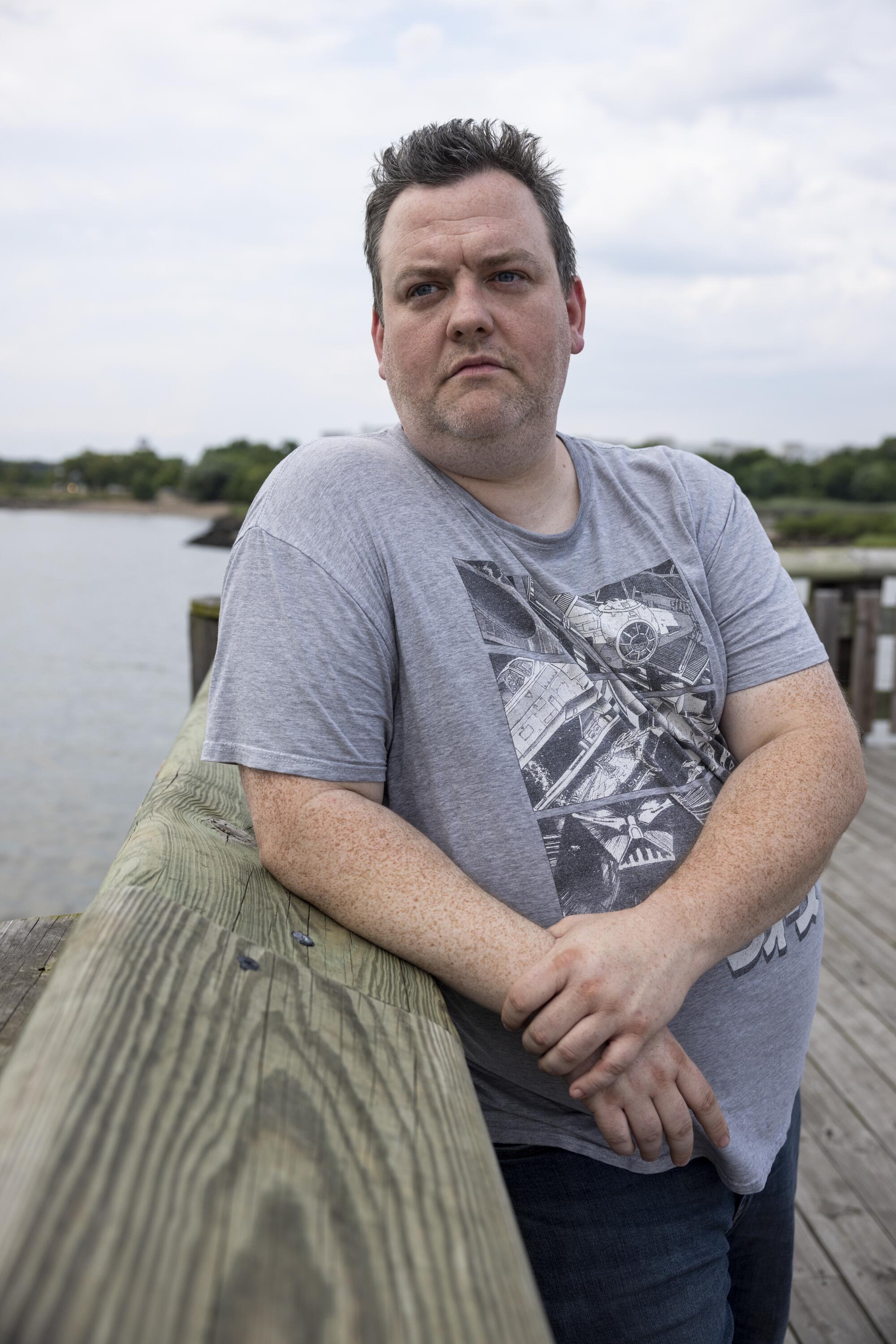 A man leans on the railing of a dock under cloudy skies.