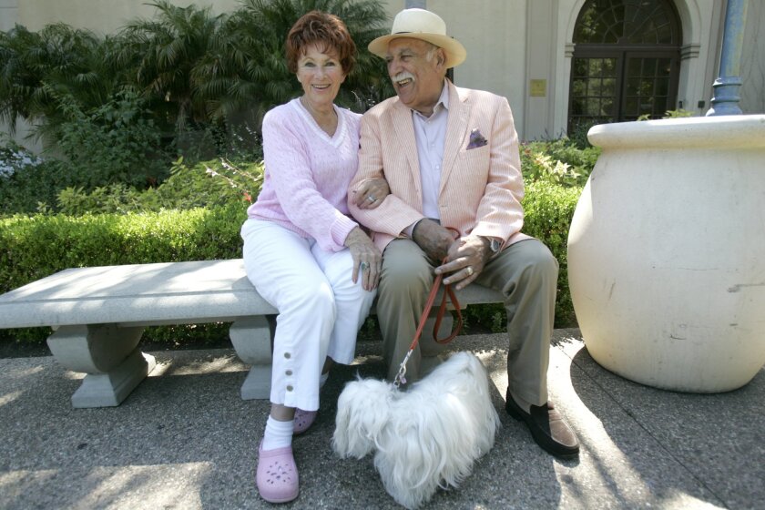 Marion Ross and Paul Michael sit on a bench in Balboa Park’s Alcazar Gardens with Blanche, the couple’s petite Coton de Tulear.