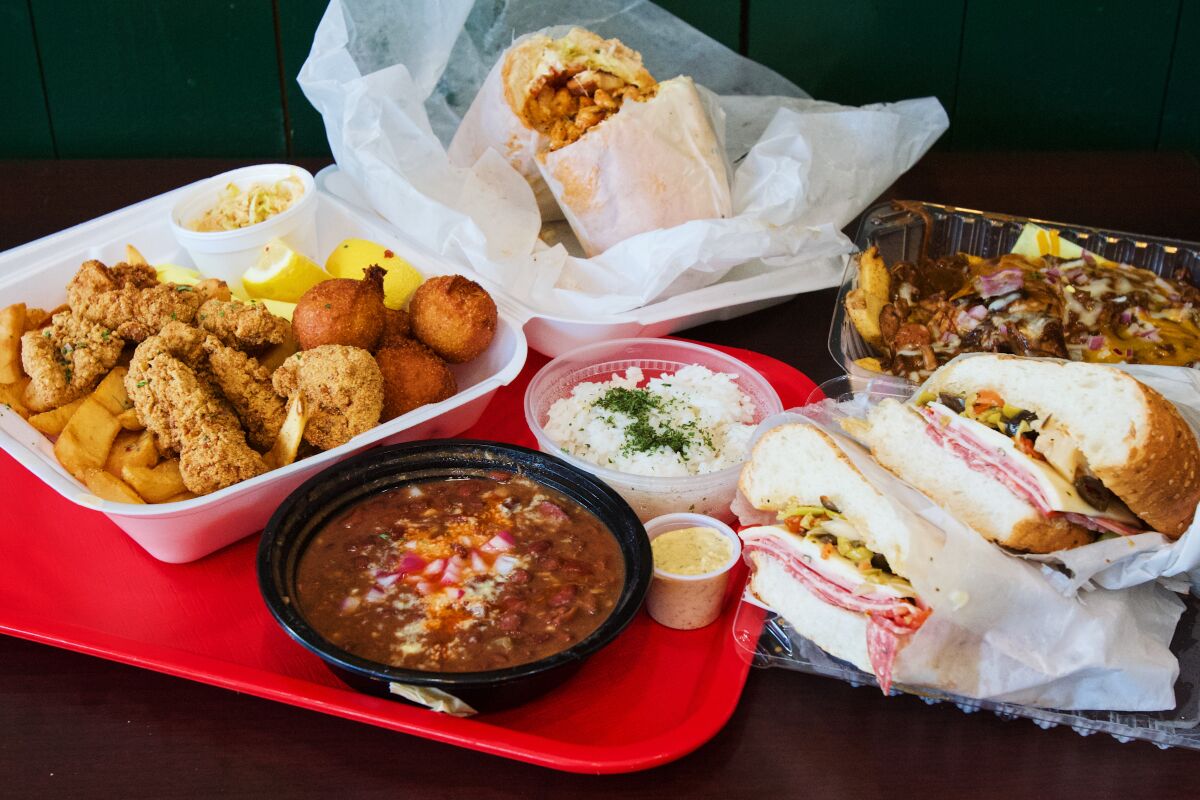 A spread of fried catfish, red beans and rice, a muffuletta, a shrimp po' boy and smothered fries rest on a red tray.