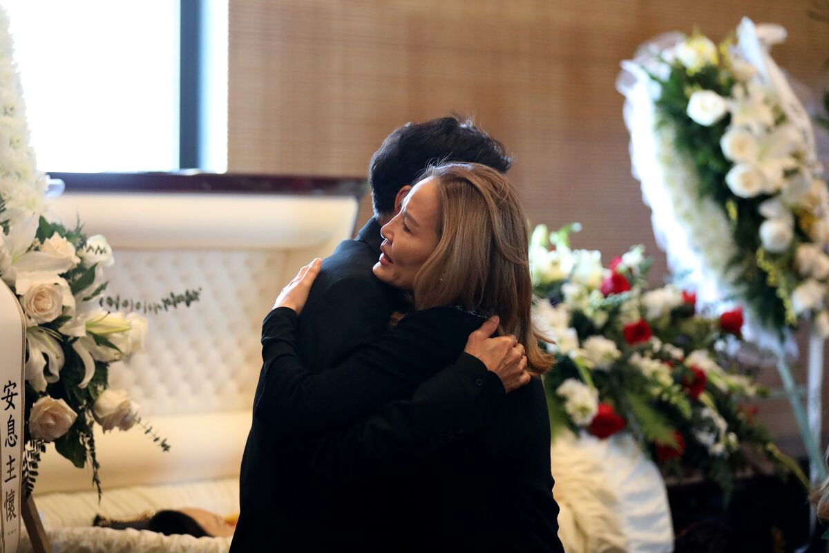 WenJu Liang, left, is consoled by a guest during the funeral service for his wife