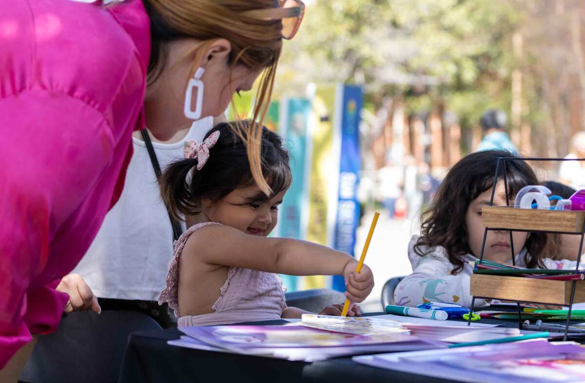 A 2-year-old girl paints with watercolors as her mom looks over her shoulder at her artwork.